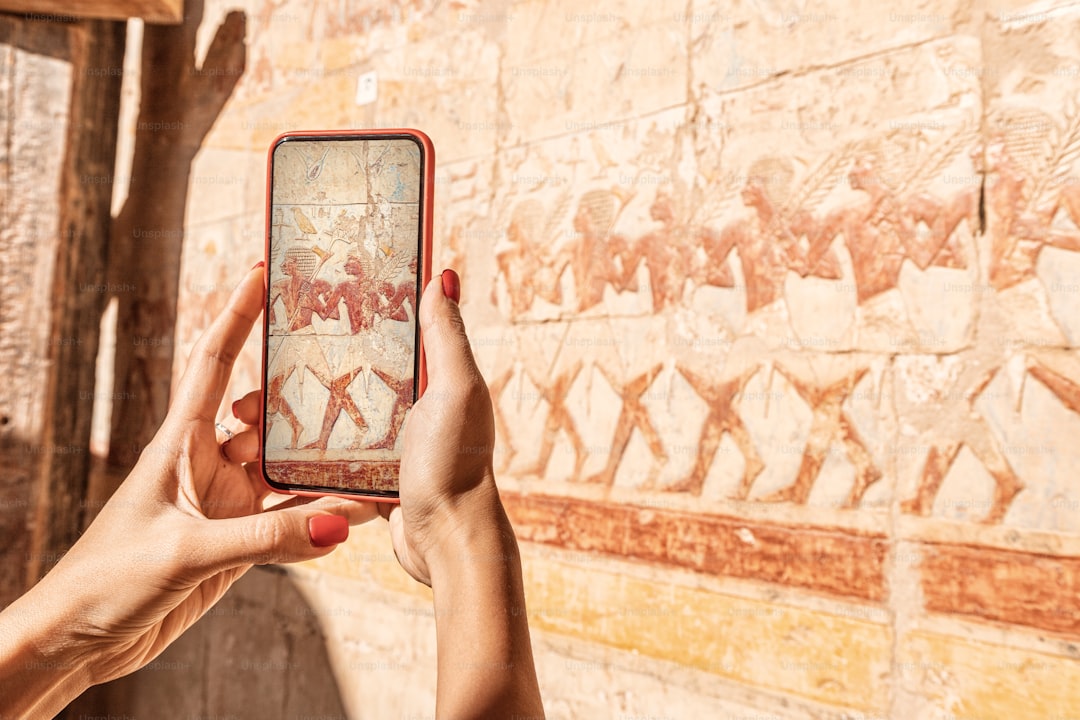 Travel blogger girl takes pictures on a smartphone at the famous Hatshepsut temple frescoes in the ancient city of Luxor in Egypt. Or using visual tourist guide